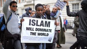 A man along with protesters standing with a poster which says: Islam will dominate the world.