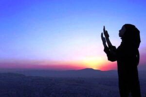 A woman in Hijab praying in front of the sunset under the open sky.